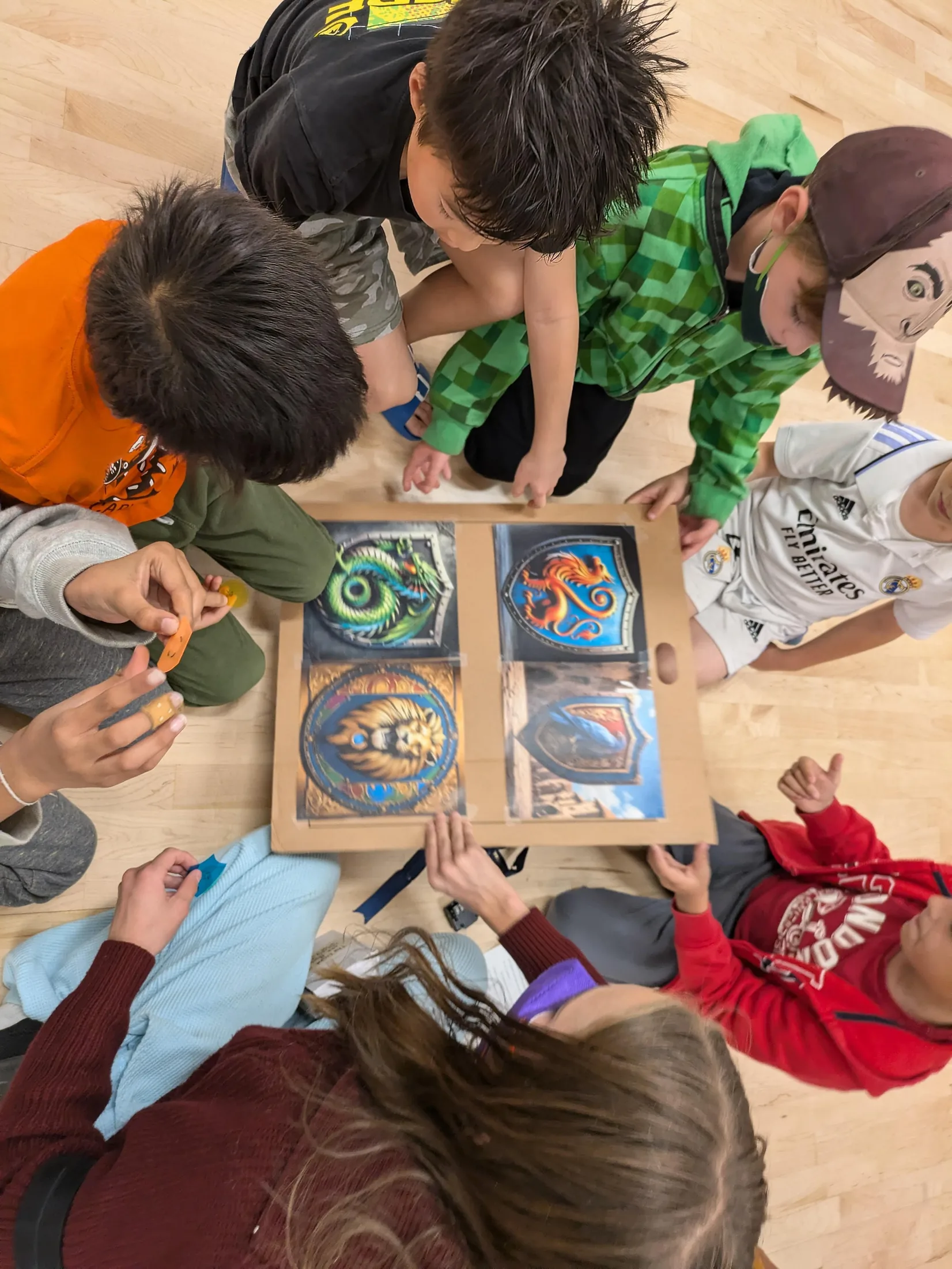 Players sitting in a circle on a gym floor around a board of clan emblems